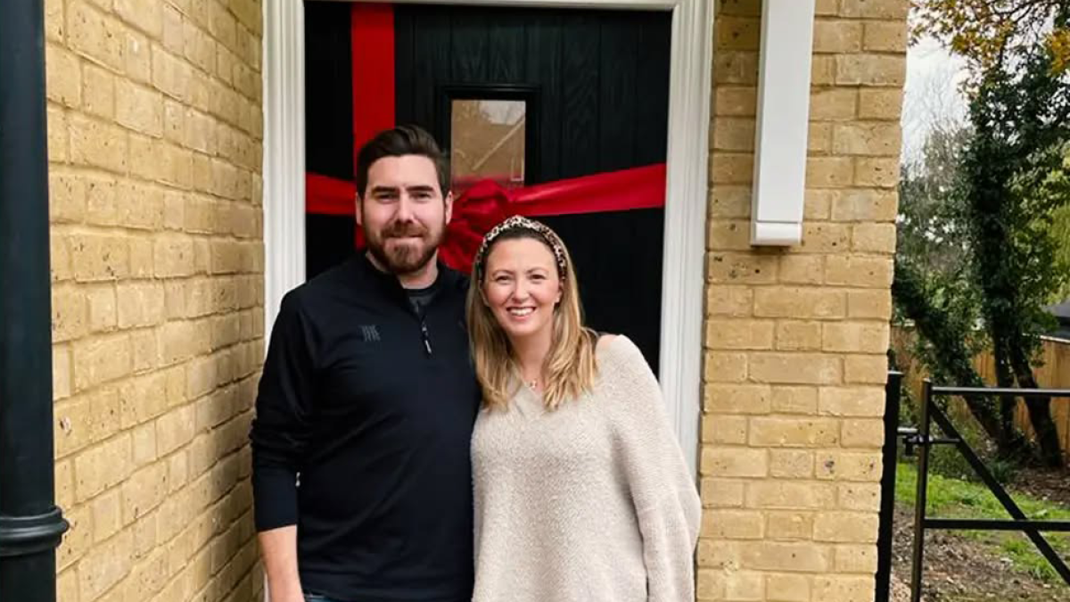 Couple outside their new home at The Meadow of Oaks, smiling by the red front door